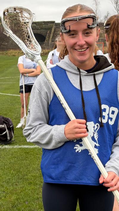 Woman holds a white lacrosse stick and wears a blue Team Scotland kit