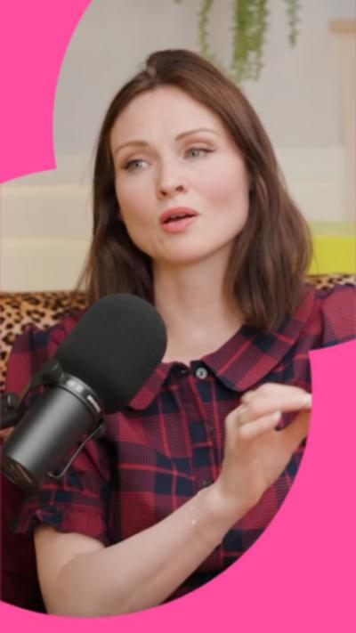 A woman with shoulder-length brown hair speaks into a microphone