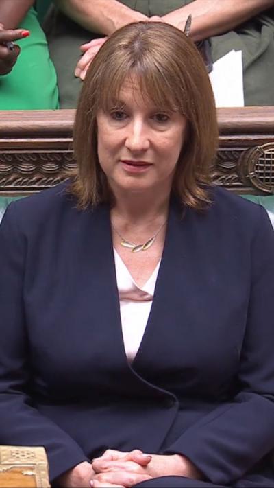 UK Chancellor Rachel Reeves wearing white blouse and navy blazer sitting in the House of Commons bench