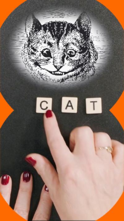A drawing of a cat's face on what looks like a chalk board with a woman's hand spelling out the word 'cat' in square counters underneath.