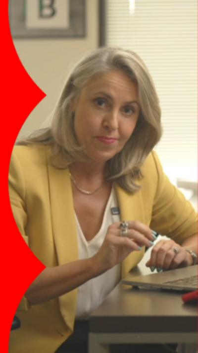 North America editor Sarah Smith wearing a yellow blazer. She's looking directly at the camera and raising her right hand.