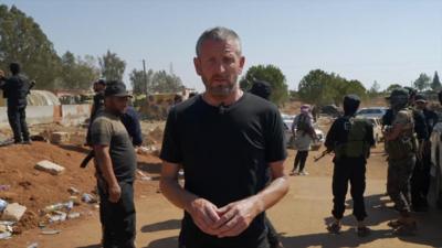 Jon Donnison stood next to men with face masks and guns