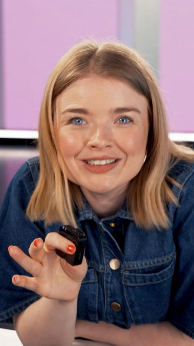 Woman with short blonde hair wearing blue denim dress and holding a small microphone