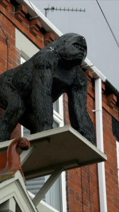 A statue of a gorilla stands on a platform attached to the top story of a terraced house