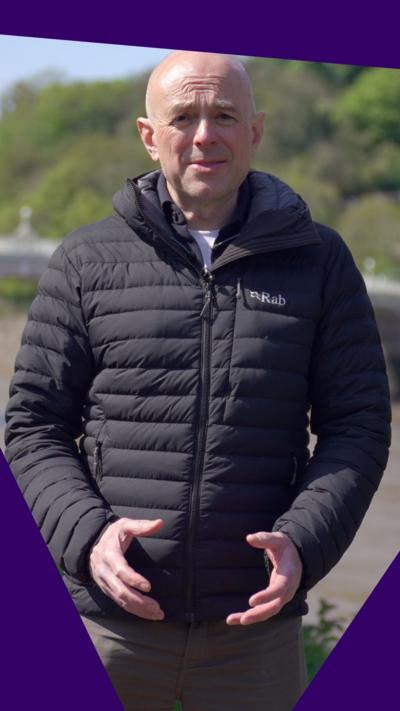 Gareth Lewis stood on a river bank in a black coat. He has a bald head