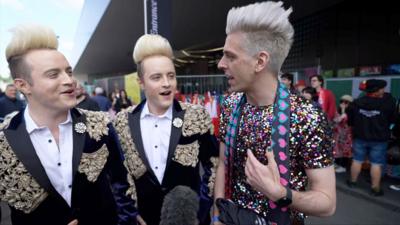 Jedward laugh as they speak to a German man with a similar hairstyle.