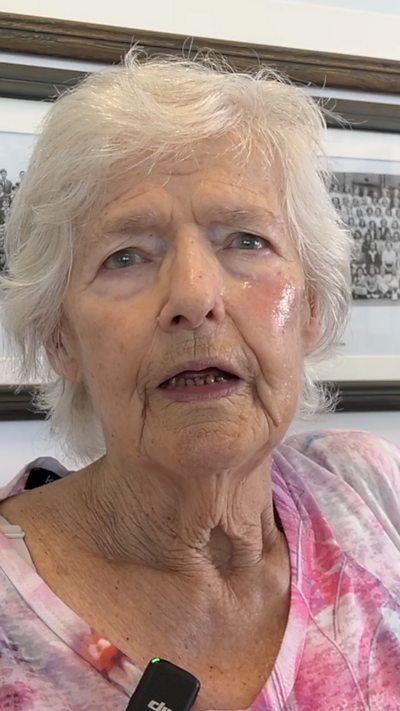 A woman in a pink top with short white hair.