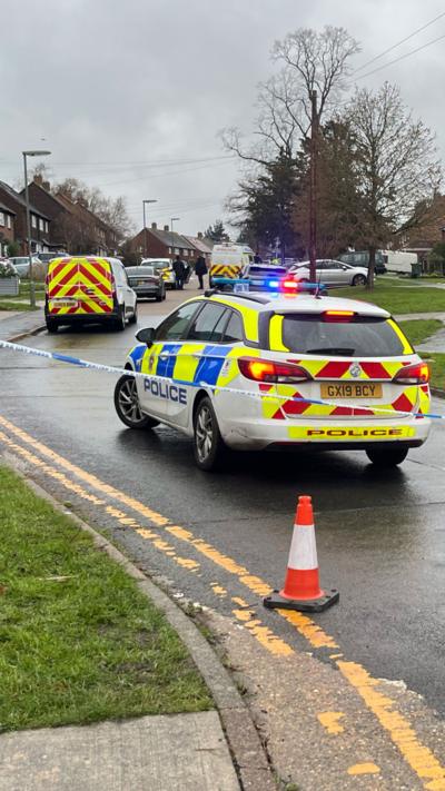 A police cordon with a marked car with its siren on.