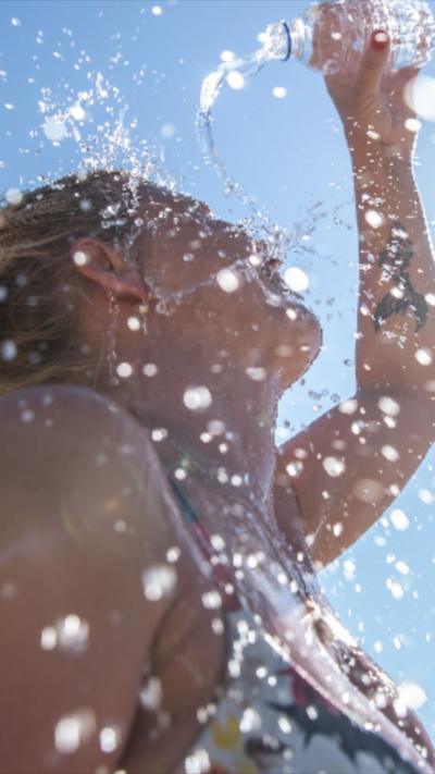 Woman pours a bottle of water over hear head as she stands in sun rays.