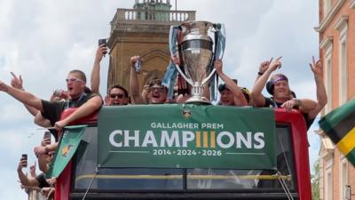 Rugby players celebrate with a huge silver trophy on an open-top red double-decker bus