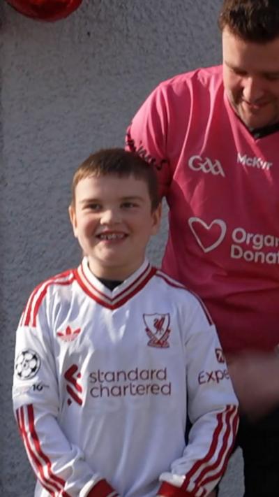 A boy stands with his father behind him. 