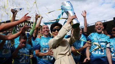 Club owner Michele Kang holding up a trophy with players from London City Lionesses