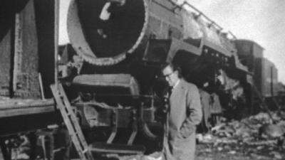 Alan Whicker stands in front of an old steam train that is being dismantled.