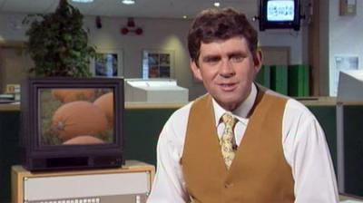 Meteorologist Philip Avery wears a yellow waistcoat. In the background, a computer displays an image of pumpkins