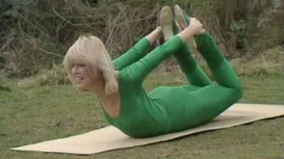 Diana Moran in a green bodysuit lying on her stomach, holding on to her ankles above her back.