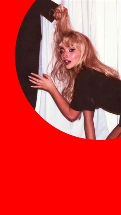 Sabrina Carpenter kneels in front of a man's legs - she has long blonde hair being held by the man, and wears a black dress
