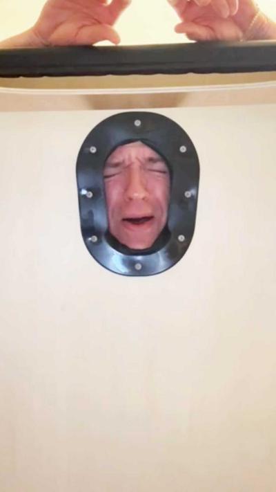 Greg looks through the hole of a massage bed in pain.