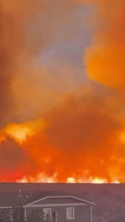 Fire is seen burning on a hill behind a row of homes.