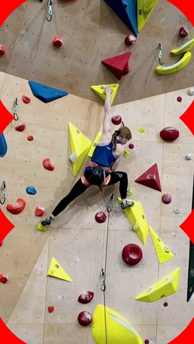 A climber, Connie Bridgens, is seen on a large indoor climbing wall with multicoloured grips