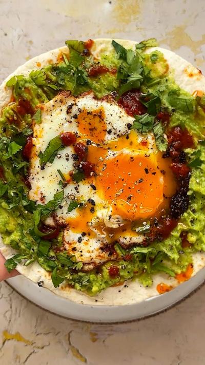 Harissa breakfast tacos with an egg in the middle, on a white plate.
