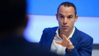 Martin Lewis gestures with his left hand while talking to someone.