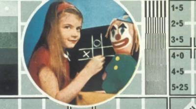 Image of young girl playing noughts and crosses alongside a clown toy