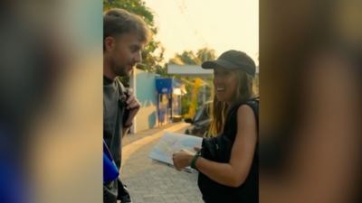 A man and a woman stands on a street in the sunshine