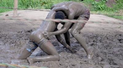 Two men covered in mud wrestle in a ring