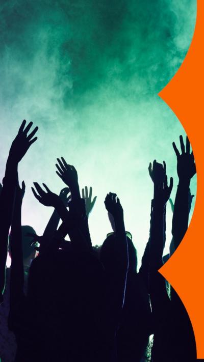 Silhouette of lots of people with arms raised dancing in a smokey room