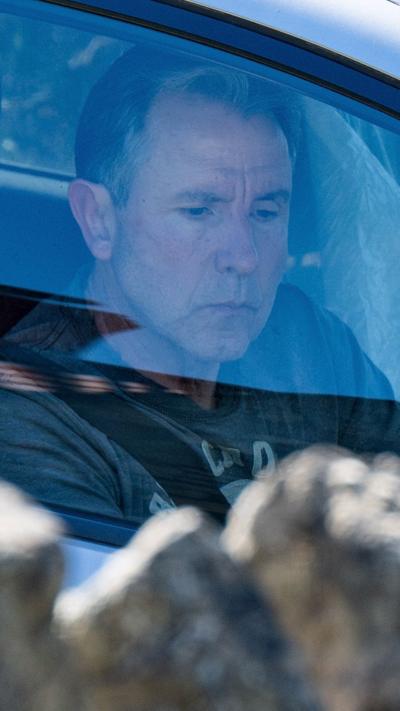 Dan Norris sat in a car looking down. He is wearing a T-shirt.