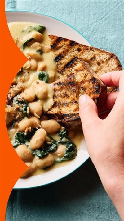 Someone dipping toast into a plate of cheesy butter beans