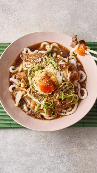 Top down view of a pair of chopsticks taking a small bit out of a bowl filled with french onion beef udon soup