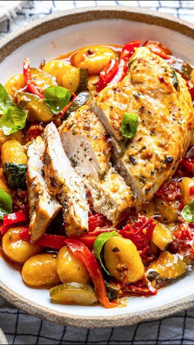 Sliced chicken breast on top of vegetables and gnocchi, on a white plate.