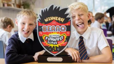 Children pulling funny faces with the Beano funniest class trophy.