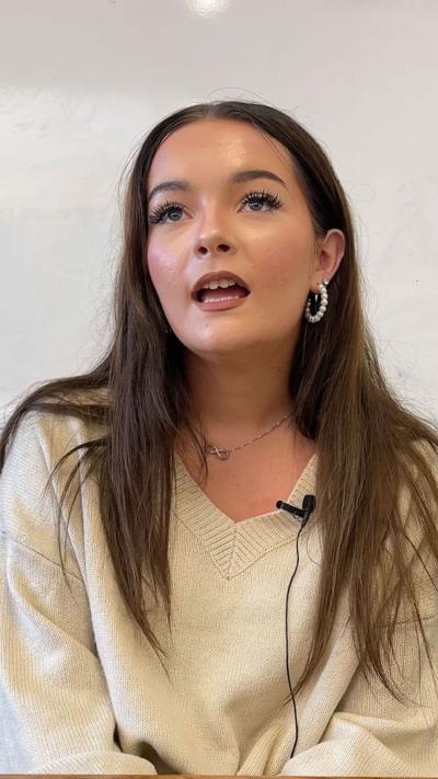 Student with long brown hair and earrings sits looking off camera as she talks