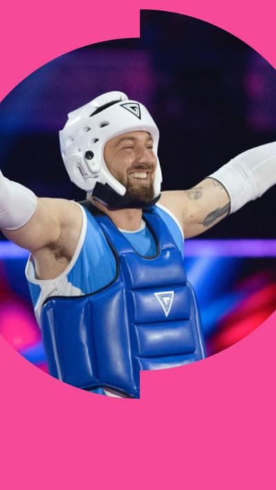 Sam Thompson in a blue kit and body protector and a white helmet smiles with his arms open