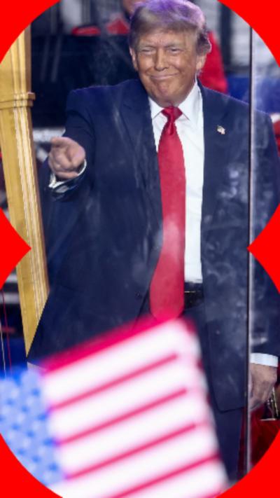 A man wearing a blue suit and a red tie points to someone off-camera