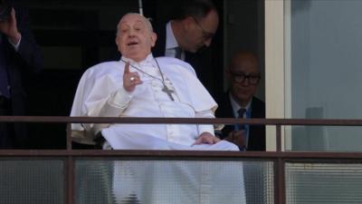 Pope Francis points as he greets crowds from a hospital balcony