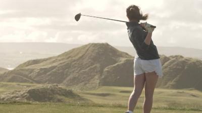 A girl tees off at golf