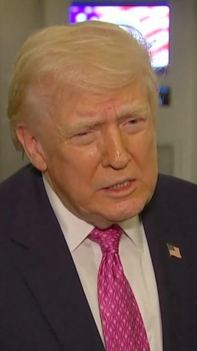 Donald Trump mid-sentence while wearing a suit and pink tie