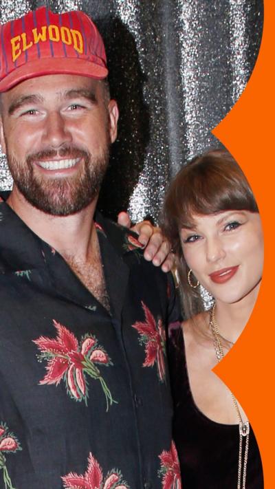Travis Kelce and Taylor Swift in a side hug in front of a silver curtain.