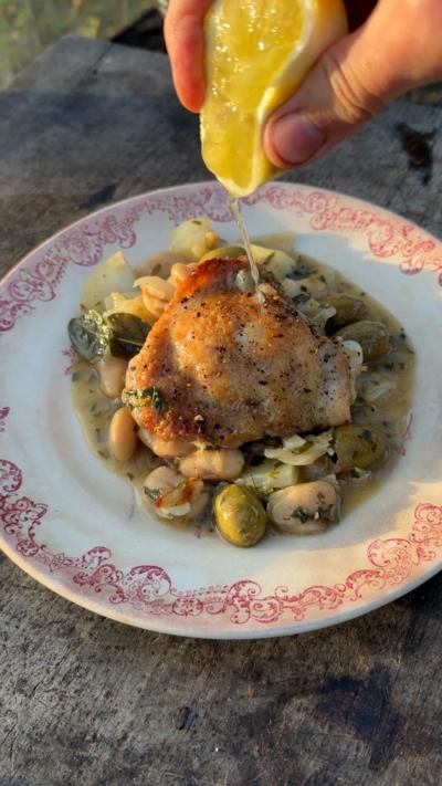 Chicken thigh on a stew of butter beans and veg on a red-rimmed plate served on a wooden table
