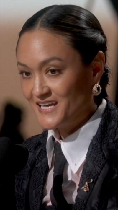 A woman with plaits wearing a shirt and tie smiles as she talks