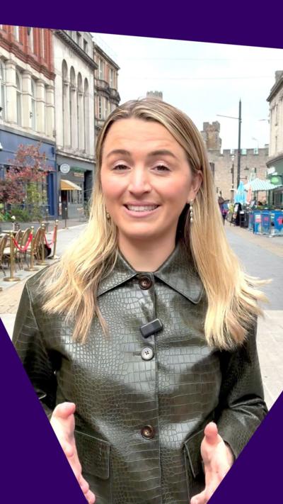 BBC's Lucy Woodham in a buttoned up leather jacket facing the camera asking a question on the streets of Cardiff.