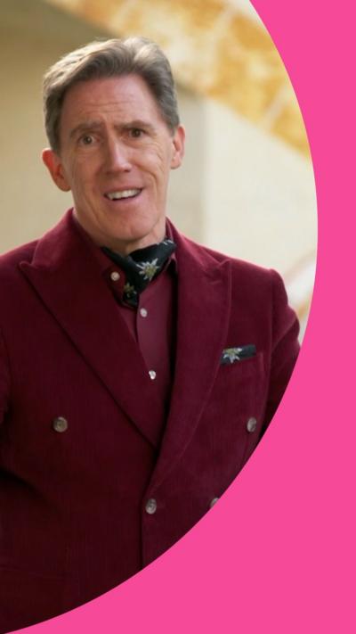 Rob Brydon dressed in a red suit and cravat, making an exasperated face to the camera
