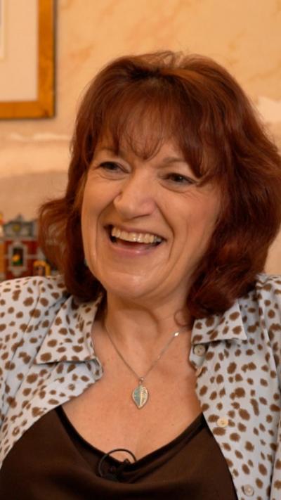 A woman with brown hair and a brown top with a grey shirt and brown spots