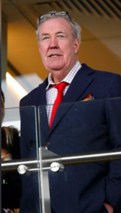 Jeremy Clarkson is wearing a navy suit, red tie, and white shirt with a black grid pattern.
