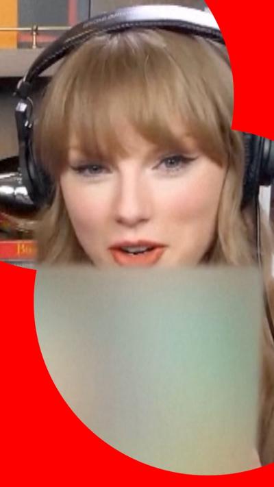 Taylor Swift holds up a copy of her new album, which is blurred out. She is sitting in a podcast studio wearing a large pair of headphones