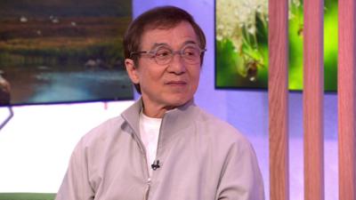 Jackie Chan wears round glasses and a beige tracksuit