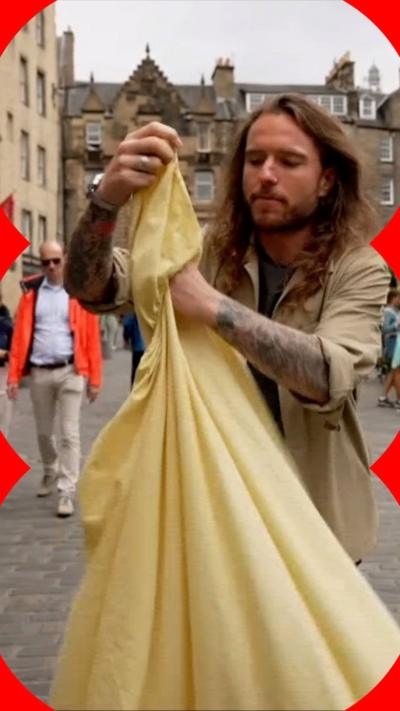 A man folding a yellow fitted sheet outdoors.